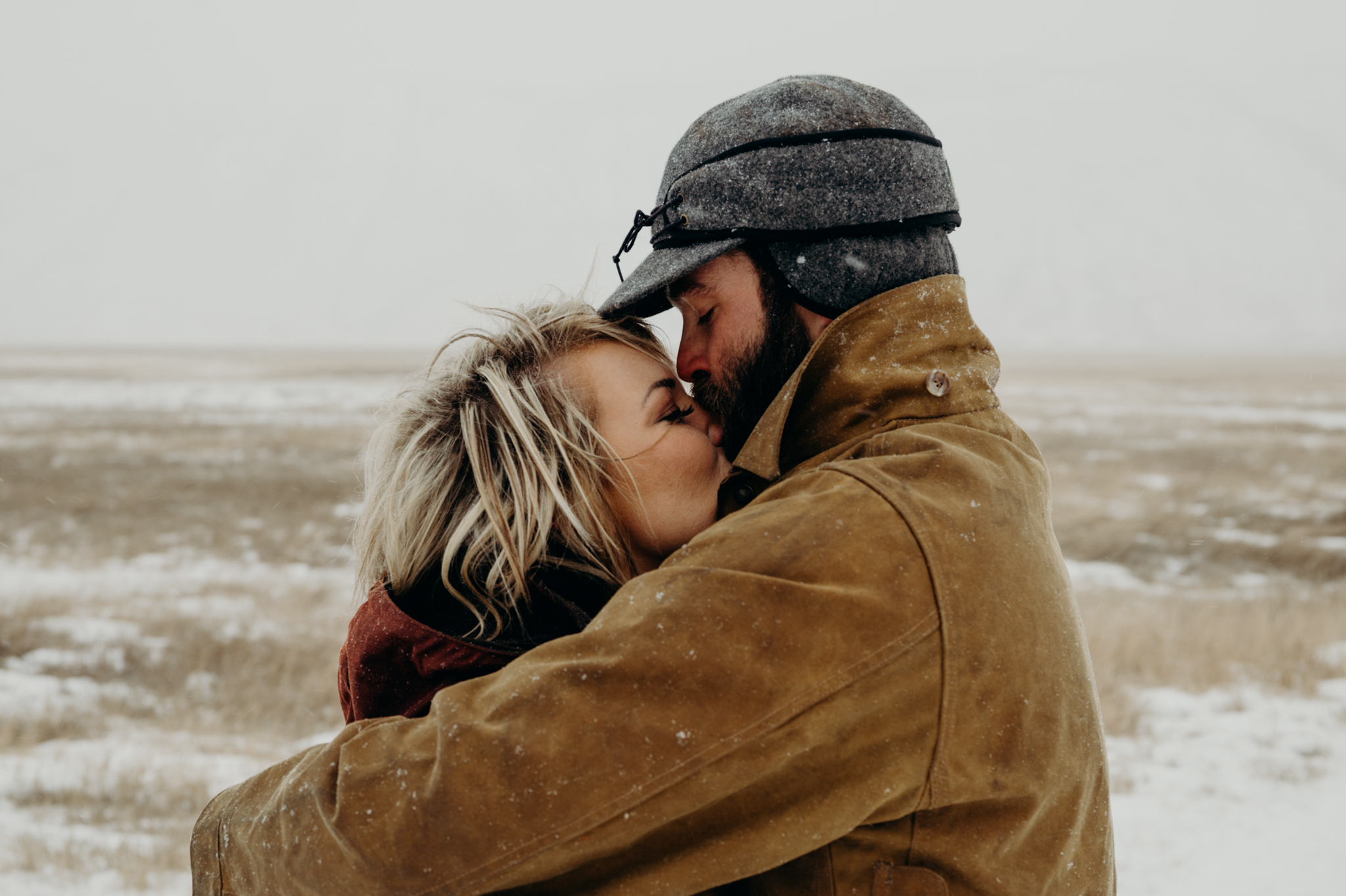 Man wearing stormy kromer and Filson jacket hugs and kisses his wife in Jackson Hole, Wyoming during a photoshoot with Erin Wheat
