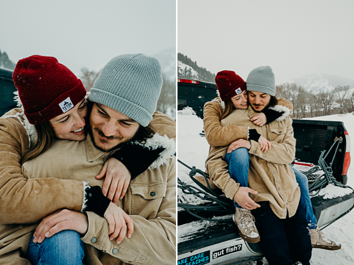 Couple wearing beanies, tan jackets, and vans embrace on the back of a truck along the Snake River in Jackson Hole Wyoming during an engagement session with Erin Wheat